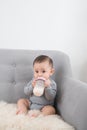 Little cute baby girl sitting in room on sofa drinking milk from bottle and smiling. Happy infant. Family people indoor Interior Royalty Free Stock Photo