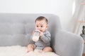 Little cute baby girl sitting in room on sofa drinking milk from bottle and smiling. Happy infant. Family people indoor Interior Royalty Free Stock Photo
