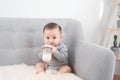 Little cute baby girl sitting in room on sofa drinking milk from bottle and smiling. Happy infant. Family people indoor Interior Royalty Free Stock Photo