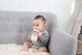 Little cute baby girl sitting in room on sofa drinking milk from bottle and smiling. Happy infant. Family people indoor Interior Royalty Free Stock Photo