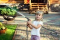 Little cute baby girl watering fresh green grass lawn mear house backyard on bright summer day. Child having fun playing with Royalty Free Stock Photo