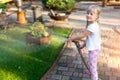 Little cute baby girl watering fresh green grass lawn mear house backyard on bright summer day. Child having fun playing with Royalty Free Stock Photo