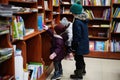 Little cute baby in jacket reaching a book from bookshelf at the library. Learning and education of european kids Royalty Free Stock Photo