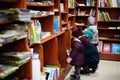 Little cute baby in jacket reaching a book from bookshelf at the library. Learning and education of european kids Royalty Free Stock Photo