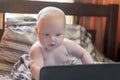 Little cute baby sitting in front of laptop in bed