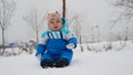 Little cute baby sitting on the snow-covered lawn in winter park