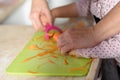 Little cute baby toddler girl in the kitchen peeling carrots with carrot peeler on chopping board. Child help at home