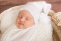 Little cute baby in a white blanket and White knitted cap in a wicker basket decorated with branches of needles and cotton