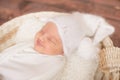 Little cute baby in a white blanket and White knitted cap in a wicker basket decorated with branches of needles and cotton