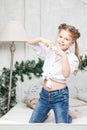 Little cute beautiful girl having fun and kneeling on the bed in blue jeans and a white shirt, showing heart and love with her Royalty Free Stock Photo