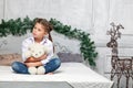 Little cute beautiful girl sits cross-legged on a bed in blue jeans and a white shirt hugging a soft teddy bear toy against the Royalty Free Stock Photo