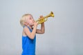 Little cute blond boy playing toy trumpet on light background Royalty Free Stock Photo
