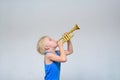 Little cute blond boy playing toy trumpet on light background Royalty Free Stock Photo