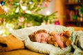 Little cute blond boy sleeping under Christmas tree and dreaming of Santa at home, indoors. Traditional Christian Royalty Free Stock Photo