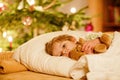 Little cute blond boy sleeping under Christmas tree and dreaming of Santa at home, indoors. Traditional Christian Royalty Free Stock Photo