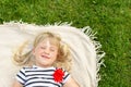 Little cute blond girl lying on blanket over green grass lawn and smiling. Adorable child having fun outdoors. Happy Royalty Free Stock Photo