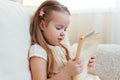 Little cute blond girl reading book siting on a sofa. Child reading, dreaming and imagination development