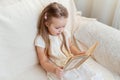 Little cute blond girl reading book siting on a sofa. Child reading, dreaming and imagination development