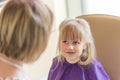 Little cute blond girl smiles and looks at hairdresser during haircut process.