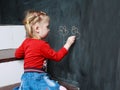 Little cute blonde girl is drawing on a blackboard Royalty Free Stock Photo