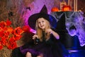 Little cute blonde girl, dressed as a witch on a gloomy background, holds a spider in her hand. Decorations for All Saints Day.