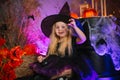 Little cute blonde girl, dressed as a witch on a gloomy background, holds a spider in her hand. Decorations for All Saints Day.