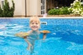 Little cute blonde girl swimming in a pool , wearing inflatable sleeves. She is smiling and happy Royalty Free Stock Photo