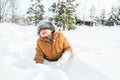 Little cute boy in black hat,orange jacket is lying,playing in snow. Kid walking in beautiful frozen forest,park among Royalty Free Stock Photo