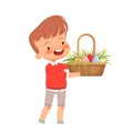 Little cute boy carries a basket with colored eggs, flowers and grass for the Easter holiday. Spring holiday Easter.