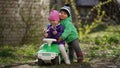 Little cute boy and girl posing on a green toy car in a park early spring