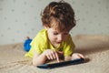 Little cute boy in a green T-shirt playing games on a tablet and watching cartoons. Toddler with tablet.