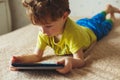 Little cute boy in a green T-shirt playing games on a tablet and watching cartoons. Toddler with tablet. Royalty Free Stock Photo