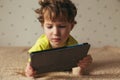 Little cute boy in a green T-shirt playing games on a tablet and watching cartoons. Toddler with tablet.