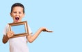 Little cute boy kid holding empty frame celebrating victory with happy smile and winner expression with raised hands Royalty Free Stock Photo