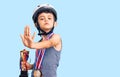 Little cute boy kid wearing bike helmet and winner medals holding winner trophy with open hand doing stop sign with serious and