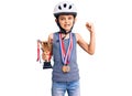 Little cute boy kid wearing bike helmet and winner medals holding winner trophy screaming proud, celebrating victory and success