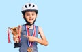 Little cute boy kid wearing bike helmet and winner medals holding winner trophy smiling happy pointing with hand and finger