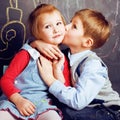 Little cute boy kissing blonde girl in classroom at blackboard, first school love, lifestyle people concept Royalty Free Stock Photo