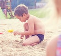 Little cute boy with plastic spatula in hand makes sand castle at the beach.