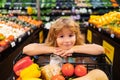 Little cute boy with shopping cart full of fresh organic vegetables and fruits in grocery food store or supermarket Royalty Free Stock Photo