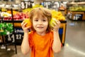 Little cute boy with shopping cart full of fresh organic vegetables and fruits standing in grocery department of food Royalty Free Stock Photo