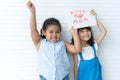 Little cute Caucasian and African girls holding handmade card together with text Love Mom, smiling and showing card Royalty Free Stock Photo