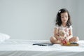 Little cute Caucasian Asian kid sitting on bed concentrating on playing small colorful xylophone with bear doll and tablet compute Royalty Free Stock Photo