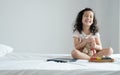 Little cute Caucasian Asian kid smiling sitting on bed playing small colorful xylophone with bear doll and tablet computer at bedr Royalty Free Stock Photo