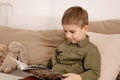 Little and cute caucasian boy reading a book on the bed at home. Interior and clothes in natural earth colors. Cozy Royalty Free Stock Photo