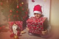 Little cute caucasian boy in Santa Claus hat sitting under Christmas tree with big red gift box, cozy home holidays and childhood Royalty Free Stock Photo