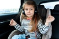 Little cute caucasian girl is driving in car.Kid listening to music with big headphones.Traveling,riding on road in safe baby seat Royalty Free Stock Photo