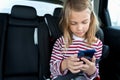 Little cute caucasian girl is driving in car. Kid writing sms, chatting, playing video games in mobile phone. Traveling on road in Royalty Free Stock Photo