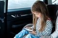 Little cute caucasian girl is driving in car. Kid writing sms, chatting, playing video games in mobile phone. Traveling on road in Royalty Free Stock Photo