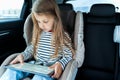 Little cute caucasian girl is driving in car. Online school learning,education.Playing video games in tablet. Traveling on road in Royalty Free Stock Photo